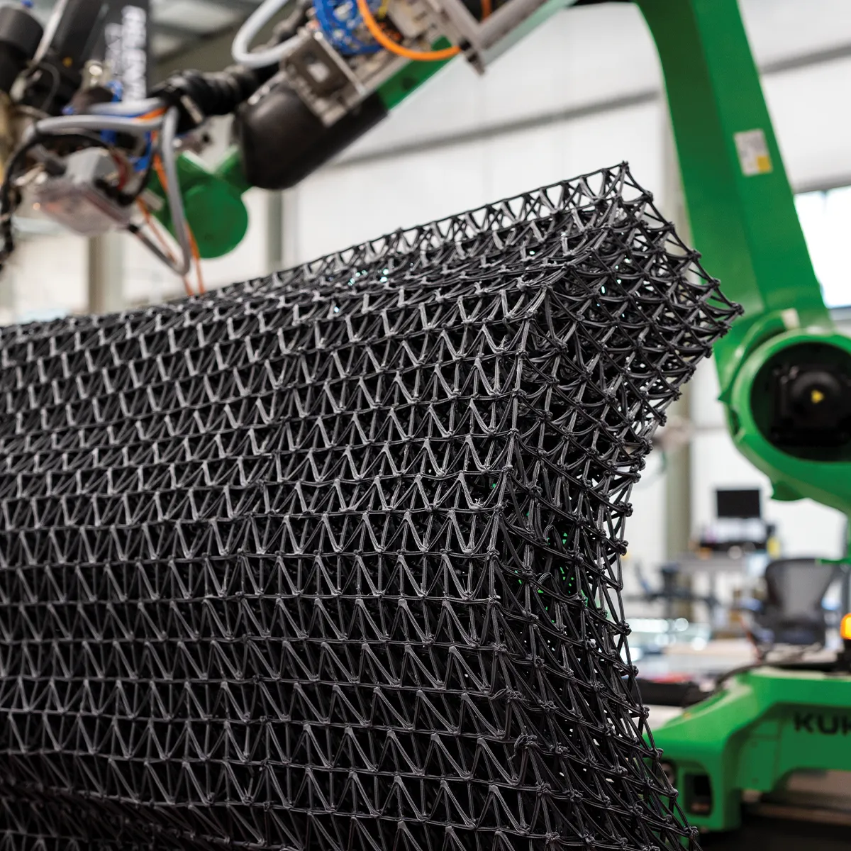 Green robot arm 3D printing a black lattice panel